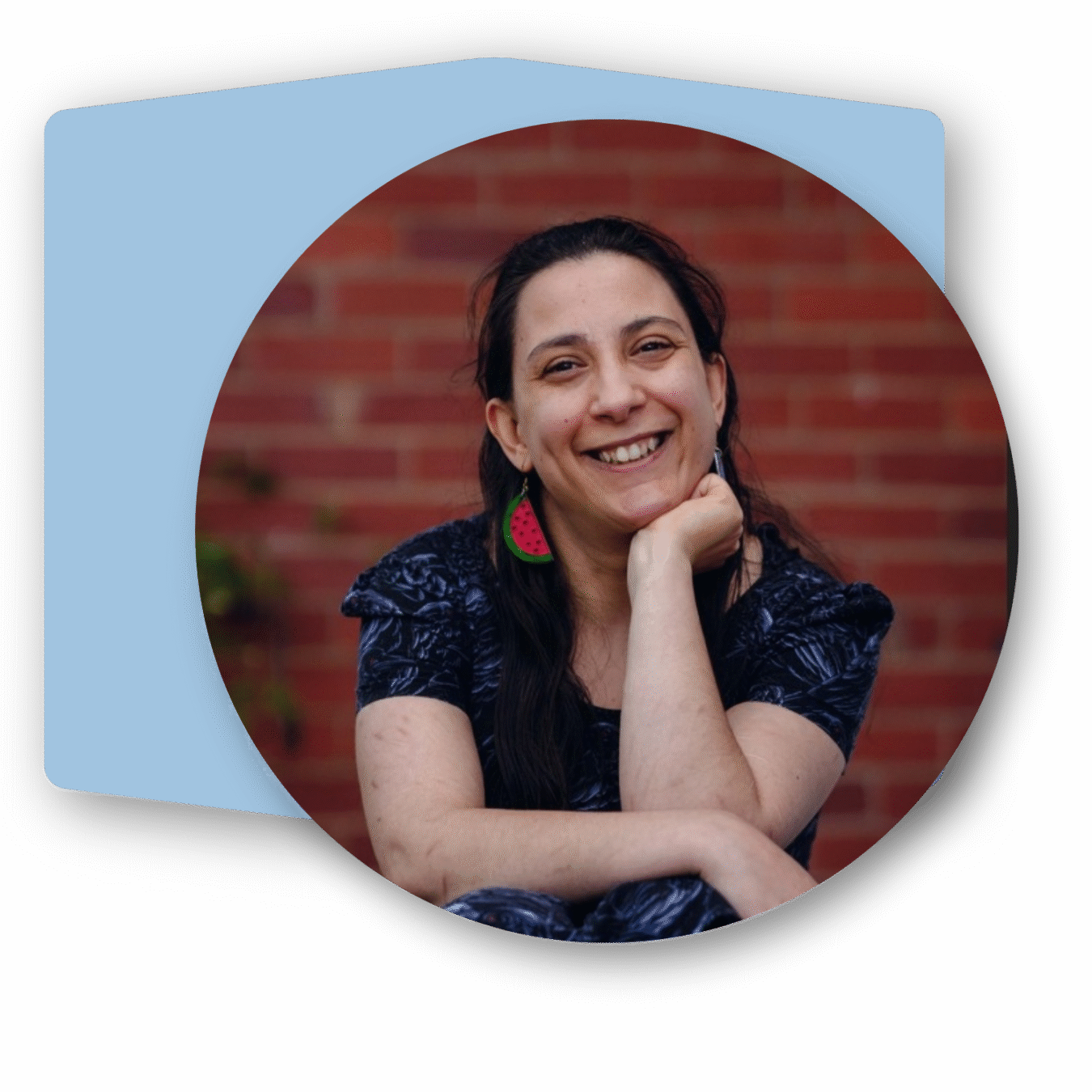 Profile picture of Laura, an Italian woman smiling at the camera. She;s wearing a dark coloured dress and watermelon earrings. Behind the photograph is a blue hexagon.